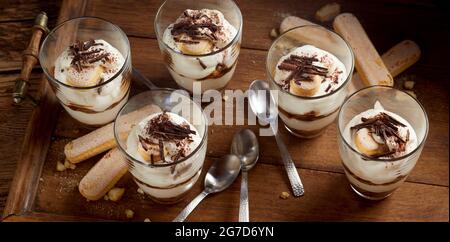 Von oben süßes Tiramisu Dessert mit geriebener Schokolade dekoriert und in Gläsern auf Holztablett serviert Stockfoto