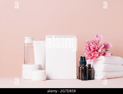 Damen Accessoires Creme Öl verschiedene Kosmetik reinigen blank Notizbuch auf einem Tisch mit Blumen. Schönheitskonzept Stockfoto