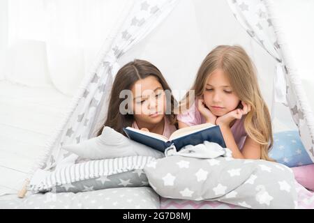 Lockdown-Ideen für Kinder. Lernen Sie weiter zu Hause. Lieblingsmärchen. Buch über Liebe. Mädchen Kinder lagen Bett lesen Buch. Angenehme Zeit im gemütlichen Schlafzimmer Stockfoto