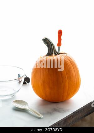 Kürbis auf einer Tischplatte mit einem Messer, das herausragt, und Werkzeugen, die umragen, bereit zum Schnitzen. Stockfoto