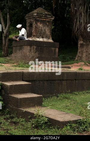 11. Juli 2021 im Dorf Mardhe, Satara, Indien. Indischer, nicht identifizierter alter Mann, der morgens vor dem kleinen Tempel sitzt, ländlicher Lebensstil. Indian Village Stockfoto