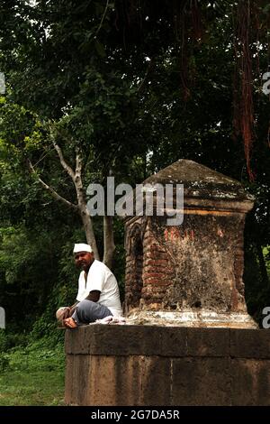 11. Juli 2021 im Dorf Mardhe, Satara, Indien. Indischer, nicht identifizierter alter Mann, der morgens vor dem kleinen Tempel sitzt, ländlicher Lebensstil. Indian Village Stockfoto