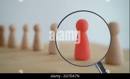 Der Blick durch die Lupe auf die eine hölzerne rote Person zwischen anderen Menschen. Ressourcenmanagement, Rekrutierung, Einstellung, Headhunting-Konzept. Finde le Stockfoto