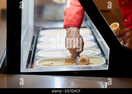 Einen Waffelkegel mit Eis füllen. Große Auswahl an verschiedenen Eiscreme. Servieren von Gelato. Stockfoto