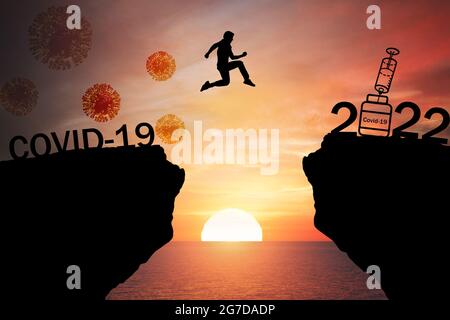 Silhouette Mann springen aus dem Berg von 2020, die covid-19 zu 2022 Jahren, die Impfung von Menschen mit dem Sonnenuntergang, Sonnenaufgang Hintergrund ausgebreitet. H Stockfoto