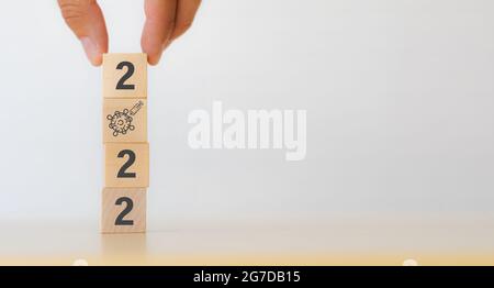 Neues Jahr 2022; das Konzept des Impfstoffs zur Prävention von Infektionskrankheiten, das man Holzwürfel mit Covid-19 oder Coronavirus von Hand auf den Tisch mit w legt Stockfoto