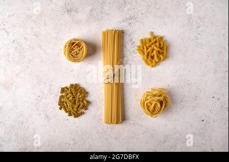 Ungekochte, rohe Gruppe von Spaghetti, Fettuccine, girandole und Tagliatelle auf grauem strukturiertem Hintergrund. Speicherplatz kopieren. Draufsicht Stockfoto