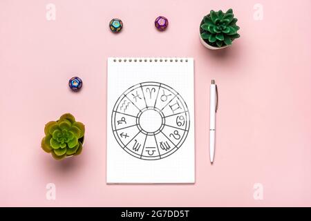 Horoskop-Kreis mit zwölf Tierkreiszeichen auf Papier, Weissagungswürfel, buntem Stein auf rosa Hintergrund Wahrsagerei und Astrologie-Vorhersagen Stockfoto