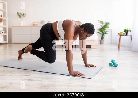 Effektive Bodyweight-Übungen. Kurvige schwarze Frau macht ein Krafttraining und läuft zu Hause mit den Händen auf dem Boden Stockfoto