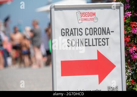 Zinnowitz, Deutschland. Juli 2021. Passanten gehen an einem Schild mit der Aufschrift „Free Corona Quick Test“ vorbei. Viele Touristen genießen Sonne, Sand, Wellen und Meer am Strand auf der Insel Usedom. Quelle: Stefan Sauer/dpa/Alamy Live News Stockfoto