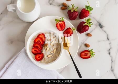 Gesunder hausgemachter Haferbrei mit frischen Erdbeeren auf weißem Marmorboden. Draufsicht Stockfoto