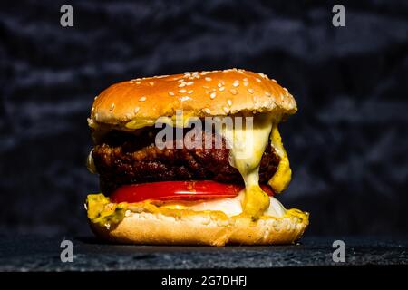 Frischer, schmackhafter Cheeseburger aus Rindfleisch mit geschmolzenem Käse auf schwarzem Hintergrund Stockfoto