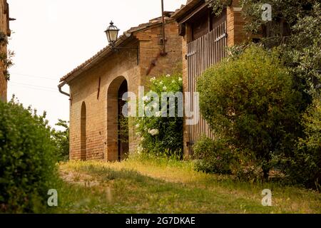 Schönes rotes Backsteinhaus in Italien, umgeben von Pflanzen und Blumen. Gemütliche idyllische Aussicht im rustikalen sonnigen Italia. Region Siena, Italien Stockfoto