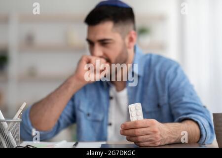 Junger Mann, der an Kälte leidet, hustet und Tabletten hält Stockfoto