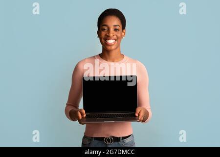 Schöne Webseite. Lächelnde Junge Afroamerikanische Frau Hält Laptop Mit Schwarzem Bildschirm Stockfoto