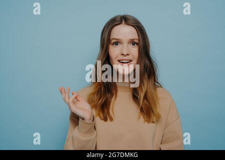 Ziemlich junges Mädchen zeigt Unterhaltung und Überraschung posiert gegen blaue Wand Stockfoto