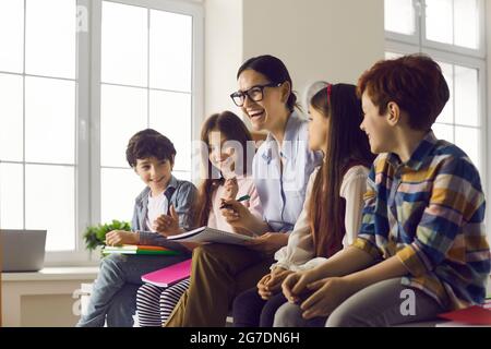 Lehrer und Schüler lachen, während sie im Klassenzimmer die Aufgabe im Textbuch überprüfen Stockfoto