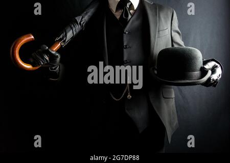 Portrait of man in Dark Suit und Lederhandschuhe mit Regenschirm und Bowler Hut auf schwarzem Hintergrund. Konzept des klassischen britischen Gentleman. Retro-Style. Stockfoto