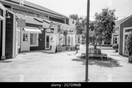 Schwarzweiß-Foto von Schaufenstern, Bäumen und einer runden Baumbank in einem kleinen Gewerbegebiet bei Larkspur Landing, Marin Country Mart, Larkspur, Kalifornien, August 15, 2020. () Stockfoto