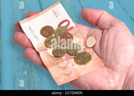 Hand mit 10 Euro Schein und kleinem Wechselgeld gegen blauen Holztisch Hintergrund Stockfoto