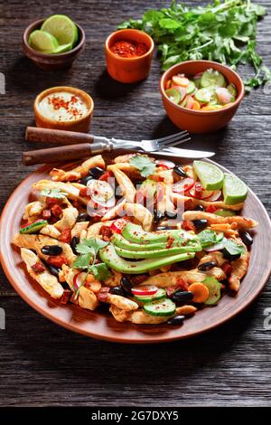 Mexikanischer Hühnersalat mit schwarzen Bohnen, Koriander, Rettich, Karotte, Gurke, Und Avocado mit Tahini-Dressing und Chili, serviert auf braunem Teller auf rustikalem Stockfoto