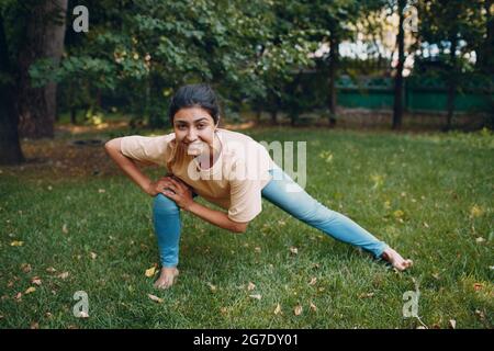 Sportliche Millennial Indian Woman in Freizeitkleidung Stretching vor dem Training im Park, Aufwärmübungen. Stockfoto