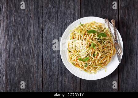 Sommer-Spaghetti alla carrettiera mit Minzblättern, Zitronenschale, Pecorino-Käse, Chilischoten-Flocken, Petersilie und geriebenen Zucchini auf einem weißen Teller Stockfoto