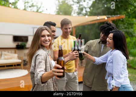 Coole junge Freunde toasten mit Bierflaschen, trinken Alkohol in der Nähe von Wohnmobil im Freien Stockfoto