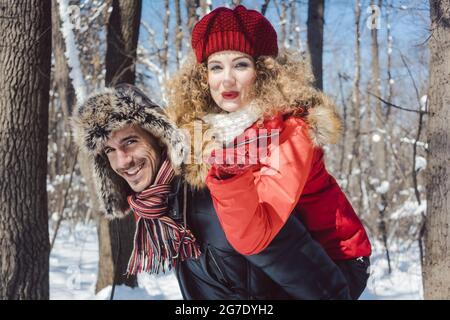 Mann, der seine Frau im Winter mit seinem Huckepack trägt, während sie einen Kuss auf die Kamera bläst Stockfoto