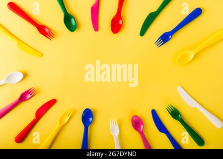 Ovaler Rahmen aus wiederverwendbarem Besteck auf gelbem Hintergrund. Plastiklöffel, Gabeln, Messer Draufsicht. Sommerpicknick. Kunststoff-Recycling-Konzept. Stockfoto