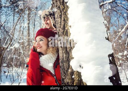 Verspieltes Paar versteckt sich hinter einen Baum im Schnee tragen warme Winterkleidung Stockfoto