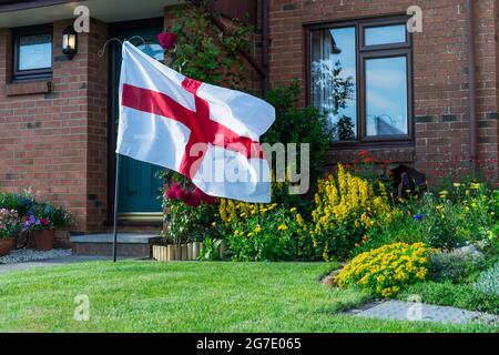 Fußballfans, die die englische Nationalmannschaft unterstützen - Fan hob die Flagge Englands auf dem Rasen in der Nähe seines Hauses. Winkende englische Flagge. Stolz auf den Nationalsport Stockfoto