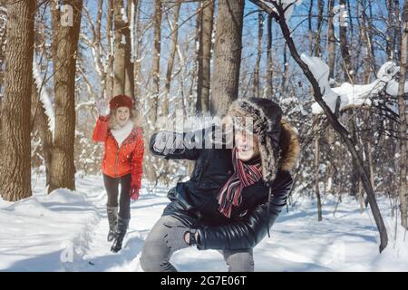 Frau, die Schneeball auf ihren Kerl im Winter in spielerischer Stimmung wirft ihn neckend Stockfoto