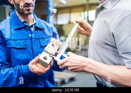 Zwei Arbeiter, die die Messungen des Werkstücks überprüfen, sind zufrieden Stockfoto