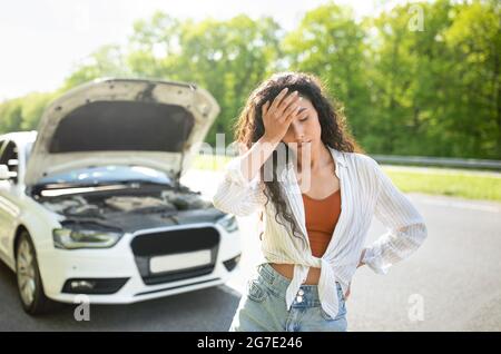 Gestresste kaukasische Frau, die auf der Straße in der Nähe ihres Autos steht, sich verloren und aufgeregt fühlt und einen Verkehrsunfall im Freien hat Stockfoto