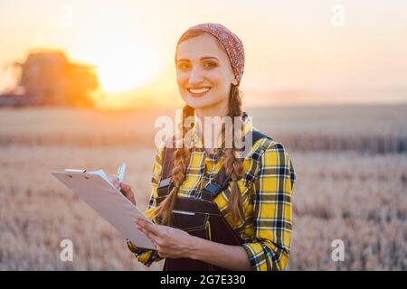 Bauer Frau und Feldhäcksler auf Weizenfeld kombinieren bei Sonnenuntergang Stockfoto