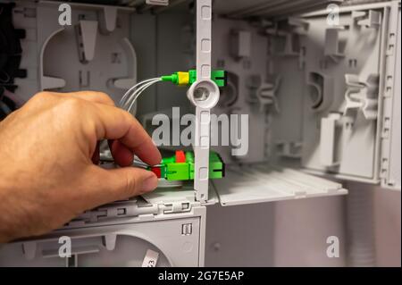 Ein Techniker bei der Arbeit: Nahaufnahme der Hand, die die Verkabelung der optischen Fasern im Verteilerkasten überprüft. Stockfoto