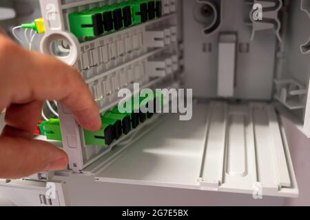 Ein Techniker bei der Arbeit: Nahaufnahme der Hand, die die Verkabelung der optischen Fasern im Verteilerkasten überprüft. Stockfoto