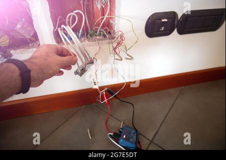 Eine Telefondose wurde geöffnet: Ein Leitungstestgerät wurde mit Klemmen verbunden. Die Hand des Technikers prüft die anderen Kabel. Stockfoto