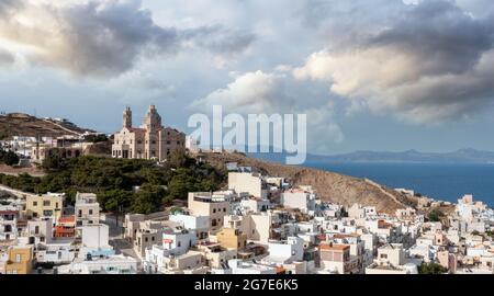 Ano Siros Stadtbild, Syros Insel, Griechenland, Luftdrohnenansicht. Die Auferstehungskirche bergauf, ruhiges Meer und wolkig blauer Himmel im Hintergrund. Stockfoto