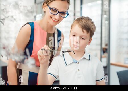 Mutter freut sich über die neue Brille ihres Sohnes, während er skeptisch und noch nicht überzeugt ist Stockfoto