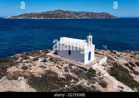 Weiße kleine Kirche auf der Insel Kimolos, Hafen Psathi, Luftdrohnenansicht. Felsige Landschaft, ruhige Ägäis, blauer Himmel im Hintergrund. Griechenland Kykladen. Sonniges wlan Stockfoto