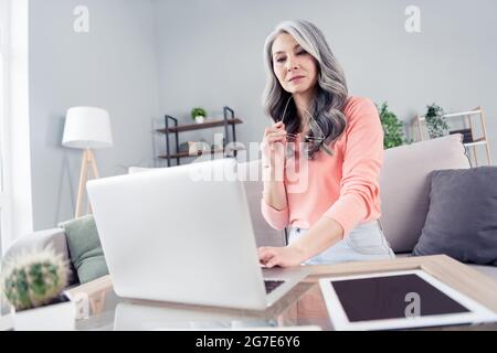 Porträt einer attraktiven, intelligent fokussierten, grauhaarigen Frau, die einen Laptop verwendet, um Präsentationen zu erstellen, die in der Wohnung im Haus eingegeben werden Stockfoto