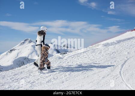 Mutter mit Kind in einem Skigebiet. Die Familie spaziert im Schnee in spezieller Skiausrüstung. Ruhen Sie sich hoch auf einem verschneiten Hang aus. Ein Mädchen führt ein Kind dazu, es zu lernen Stockfoto