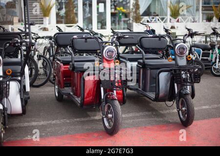 Moto-Elektrofahrzeuge sind in einer Reihe. Verleih von Elektrofahrrädern. Scheinwerfer an Fahrzeugen mit zwei Rädern. Motorradverkauf. Massenparkplätze für Fahrzeuge. Modern urban Stockfoto