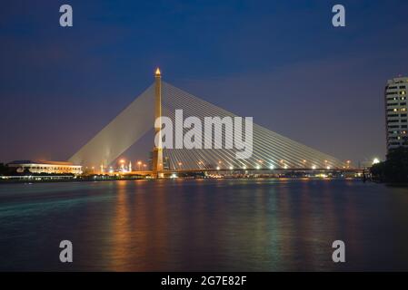 Blick auf die Seilbrücke Rama VIII Brücke am Chao Phraya Fluss in der Abendbeleuchtung. Bangkok, Thailand Stockfoto