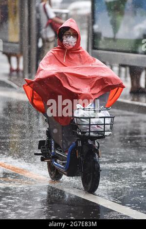 Peking, China. Juli 2021. Eine Frau in einem Regenmantel sah während des Regensturms ein Elektrofahrrad fahren. Peking ergriff am Montag mehrere Maßnahmen, um den heftigsten Regen zu bewältigen, der die Hauptstadt dieses Jahr getroffen hat. Kindergärten, Grund- und weiterbildende Schulen in der Stadt haben am Montag den Unterricht ausgesetzt, und die Mitarbeiter des Unternehmens wurden aufgefordert, von zu Hause aus zu arbeiten oder ihre Reisezeit zu ändern. (Foto von Sheldon Cooper/SOPA Images/Sipa USA) Quelle: SIPA USA/Alamy Live News Stockfoto