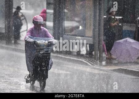 Eine Frau, die einen Regenmantel trägt und während eines Regensturms in Peking mit einem Elektrofahrrad fährt. Peking ergriff am Montag mehrere Maßnahmen, um den heftigsten Regen zu bewältigen, der die Hauptstadt in diesem Jahr traf.Kindergärten und Grund- und Sekundarschulen in der Stadt haben am Montag den Unterricht ausgesetzt und Mitarbeiter des Unternehmens wurden dazu ermutigt, von zu Hause aus zu arbeiten oder ihre Reisezeit zu ändern.Studienreisen und andere Outdoor-Gruppen Die Aktivitäten wurden entmutigt.die Pekinger Wasserbehörde erließ am Sonntag um 2 Uhr eine Stufe-III-Notflutreaktion, die erste ihrer Art in diesem Jahr. Peking ergriff am Montag mehrere Maßnahmen Stockfoto