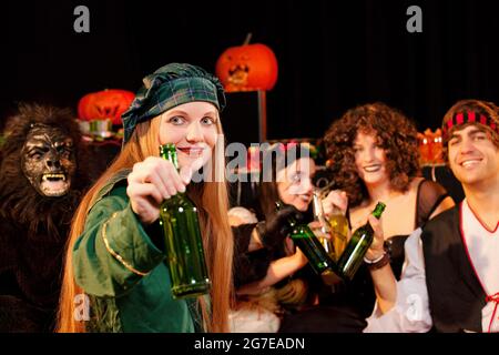 Eine Gruppe junger Menschen feiert einen Karneval oder eine Halloween Party in Kostümen und trinkt Bier Stockfoto