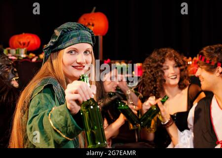 Eine Gruppe junger Menschen feiert einen Karneval oder eine Halloween Party in Kostümen und trinkt Bier Stockfoto